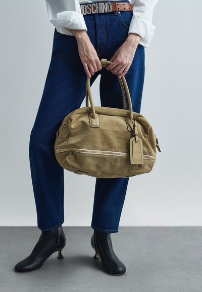 Beżowa torebka z zamszu z podwójnymi uchwytami u góry, z teksturowaną powierzchnią i przednią kieszenią na zamek. Zawiera odpinaną metkę do identyfikacji.