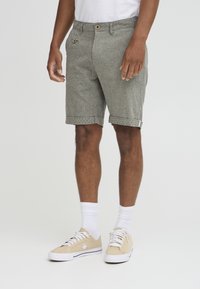 Pantaloni corti gessati grigi con chiusura a bottone, tasca frontale e risvolti, abbinati a sneaker chiare e calze bianche.