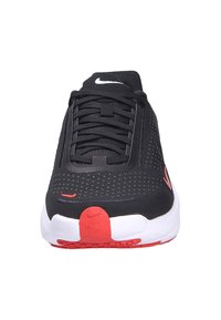 Zapatilla negra con una parte superior texturizada, suela blanca, acentos rojos en el talón y un sistema de cordones negro. Logo de Nike en blanco en la lengüeta.