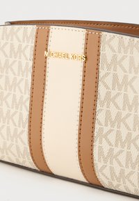 Michael Korsi kott, mis on beeži ja pruuni värvigamma, tekstureeritud kangas logomustriga ning kuldse tooniga brändiembleemiga.