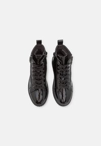 Črne lakaste usnjene visoke teniske z bočnim zadrgo, sprednjimi vezalkami in gumijastim podplatom. Imajo gladko, sijočo teksturo in zanke.