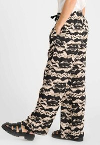 Pantalons à jambes larges en noir et beige à motif, fabriqués en tissu léger, avec une taille élastique et des poches latérales.