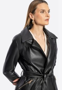 Czarny skórzany płaszcz trench z dużym kołnierzem, związanym w talii, bocznymi kieszeniami na zamek i gładką teksturą. Charakteryzuje się eleganckim, dopasowanym fasonem.