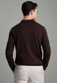 Pullover in magenta a maglia con colletto strutturato, maniche lunghe e orlo a coste, abbinato a pantaloni chiari con tasche posteriori.