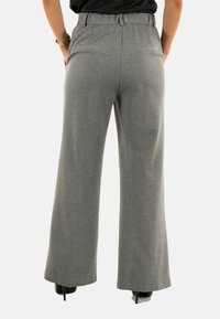 Pantaloni grigi a gamba larga realizzati in un morbido tessuto con una finitura liscia. Presentano una vita alta, tasche laterali e tasche posteriori visibili.