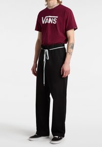 T-shirt bordeaux Vans con logo bianco, abbinata a pantaloni neri con vita elastica e cordino azzurro chiaro, indossata con scarpe nere.