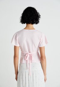 Roze katoenen t-shirt met korte flapmouwen en een strik aan de achterkant, gecombineerd met een lichte, met een patroon versierde rok met blauwe accenten.