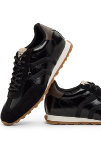 Ζευγάρι μαύρα sneakers χαμηλού προφίλ με καφέ λεπτομέρειες, λευκές ενδιάμεσες σόλες, υφασμένες σόλες και κλείσιμο με κορδόνια σε λευκό φόντο.