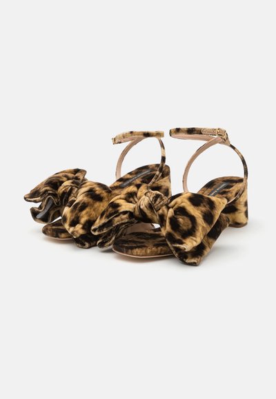 Sandale din catifea cu imprimeu de leopard, cu un accent de fundă lată, bretea la glezna și toc pătrat. Textură moale și scheme de culori maro-negru.