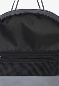 Pilkos tekstūros maišo vidus su juodu tinklu ir užtrauktuku. Lupenų konstrukcija ir sklandi tekstūra. Vertikalios baltos juostos palei kraštą.