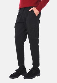Pantaloni cargo neri in cotone con tasche laterali, design affusolato e texture liscia, abbinati a scarpe in suede nere.
