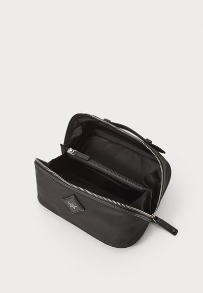 Bolsa de tecido preto com fecho de correr. O interior apresenta um compartimento principal e uma seção menor com fecho. Textura suave, sem padrões decorativos.