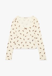 Langærmet creme top i ribbet stof med et teddy-bear print og en dekorativ brun sløjfe ved halsudskæringen. Scallopede kanter pryder designet.