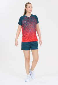 Sportig atletisk outfit med en kortärmad tröja i gradientmönster i röd och teal samt matchande teal shorts. Inkluderar logotypdetalj på tröjan.