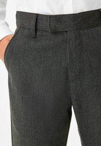 Pantalon gris sur mesure en tissu texturé, avec une coupe plate à l'avant, des poches latérales et une silhouette ajustée.