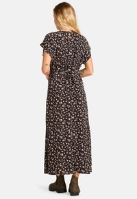 Vestido maxi floral negro, con mangas cortas y flotantes, cintura ceñida y diseño fluido con un patrón disperso en rosa y blanco.