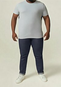 Grå T-shirt med korta ärmar, kombinerad med mörkblå slim fit-jeans. Modellen bär vita slip-on-skor och visar upp en avslappnad outfit.