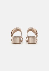 Metallic gold heeled sandals with open back, adjustable strap, and a low block heel. Smooth texture, minimalist design, and no embellishments.