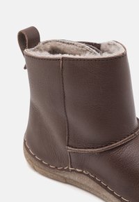 Botte cheville en cuir marron avec un intérieur doux, des coutures décoratives et une petite languette à l'arrière pour un enfilage facile.