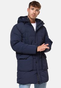 Geacă puffer de culoare bleumarin, cu glugă, având un fermoar frontal, buzunare mari aplicate și o textură quilted. Proiectată pentru căldură și confort.