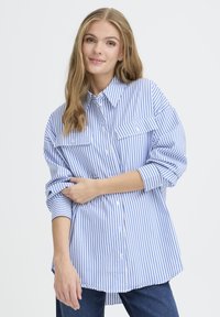 Blue and white striped button-up shirt with long sleeves, two front pockets, a collar, and a slightly curved hem. Textured cotton fabric.