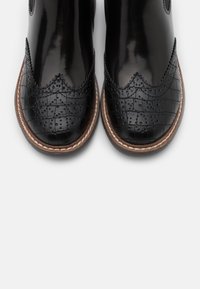 Black leather ankle boots with a glossy finish, featuring textured croc patterns, decorative stitching, and a brown rubber sole.