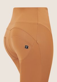 Leggings high-waisted color pesca realizzati in un tessuto liscio ed elastico, con linee di cucitura decorative e un piccolo accento con logo nero.