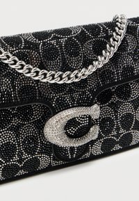 Μαύρο τσαντάκι με χάντρες και λαμπερή μαύρη υφή, με αλυσίδα λουρί από ασημί μέταλλο και κούμπωμα με διακοσμητικό λογότυπο από στρας.