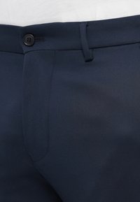 Pantaloni tailored blu navy realizzati in tessuto liscio, con chiusura a bottone, davanti piatto e tasche laterali con cuciture rifinite con cura.