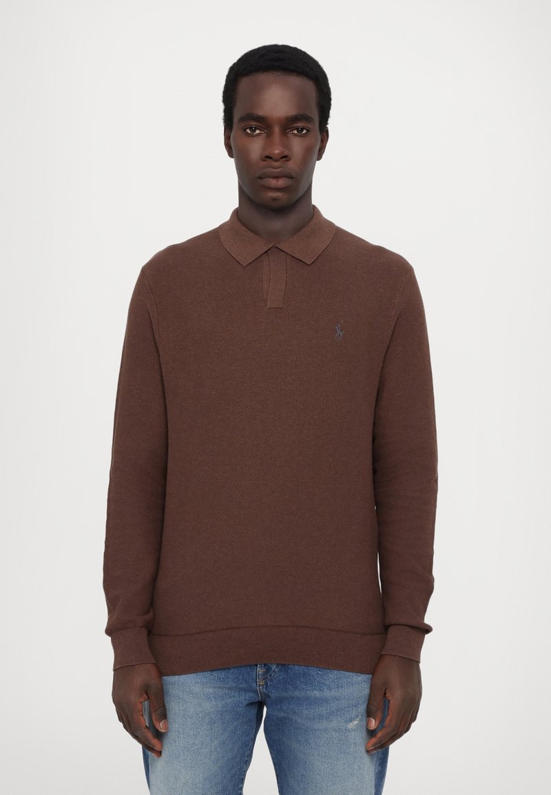 Brun langærmet polo skjorte med struktureret stof, kravehals og et lille logo på brystet. Sammen med lys blå denim jeans.