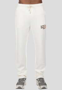 Witte sweatpants met een trekkoordsluiting, zijzakken en "WRONG FRIENDS" in bruin geborduurd op de linker bovenbeen. Gestructureerde stof.