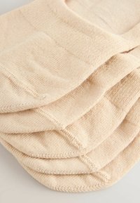 Mīkstas bēšas adītas zeķes sakrautas, parādot ribotu tekstūru un stitched pirkstus uz gaismas virsmas.