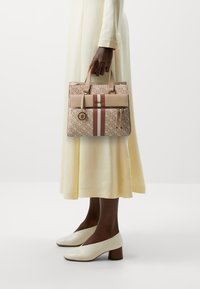 Beżowa torebka wzorzysta z dwoma uchwytami, jasnoróżowym paskiem, złotymi akcentami i detalem w postaci frędzli. Wykonana z miękkiej skóry i o sztywnej formie.