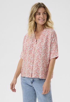 Blusa a maniche corte di colore rosa chiaro con motivi floreali sparsi in rosso e blu; presenta un collo a V e una chiusura con bottoni davanti.