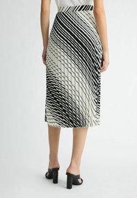 Falda plisada de longitud media en blanco roto con rayas diagonales en negro. Combinada con sandalias de tacón cuadrado en negro con un acento texturizado.