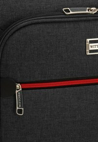 Sac à dos en tissu noir avec accent de fermeture éclair rouge. Caractéristiques d'un design épuré, d'un matériel en métal et d'une plaque logo. Matériau texturé.