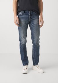 Blå denimjeans med raka ben, med subtila blekningar och slitningar. Bärs med vita sneakers och en svart t-shirt.