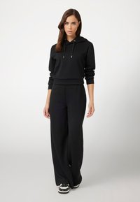 Felpa nera con cappuccio e dettagli dorati abbinata a pantaloni larghi, entrambi realizzati in un morbido tessuto. Completato con sneakers in bianco e nero.