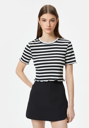 Stribet crop top i sort og hvid med ribbet tekstur, rund halsudskæring, korte ærmer og flæsekant. Sammen med en høj taljeret sort nederdel.