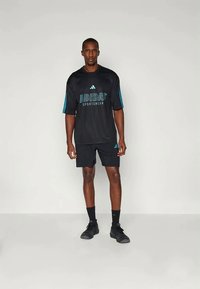 Conjunto desportivo Adidas preto, com uma camiseta de manga curta com detalhes azuis e logótipo, emparelhado com calções pretos e sapatilhas atléticas pretas.