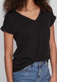 Černé tričko s V- výstřihem a ohrnutými krátkými rukávy, vyrobené z měkké látky, s volným střihem, kombinované s modrými džíny.