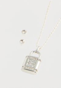 Colier cu pandantiv în formă de lacăt argintiu, decorat cu email și gravat cu "DK NY", accentuat de cristale transparente. Include cercei asortați tip studs.