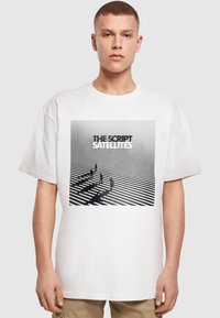 Hvid bomulds t-shirt med et grafisk print, der viser sort og hvid striber, silhuetter og teksten "THE SCRIPT SATELLITES."