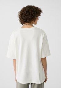 T-shirt bianco oversize con maniche corte e scollatura rotonda, caratterizzato da una texture morbida. Sfondo neutro per contrasto.