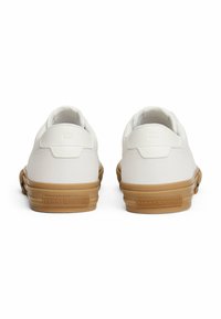 Zapatillas de cuero blancas con una textura suave, suela de goma y logotipo en relieve "TOMMY HILFIGER" en la parte posterior. Diseño redondeado.