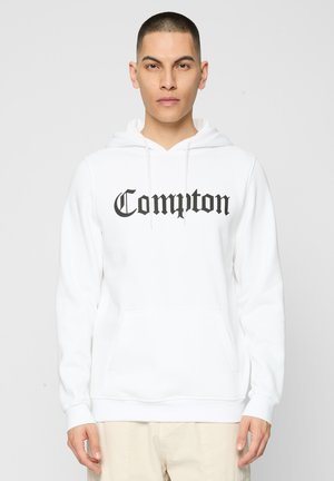 Fehér pamut kapucnis pulóver elülső zsebbel, húzózsinórral ellátott kapucnival, és fekete, dőlt betűtípussal írt "Compton" felirattal. Ribbelt mandzsettákkal és alsó szegéllyel rendelkezik.