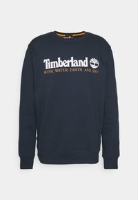 Laivastonsininen collegepaita, joka on valmistettu puuvillasekoitteesta. Siinä on pyöreä pääntie, resorit hihansuuissa sekä valkoinen Timberland-logo ja teksti kontrastivärissä oranssina.