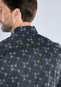 Schwarzes Hemd mit wiederholtem weißem Wellenmuster, spitzem Kragen und durchgehendem Knopfverschluss auf der Rückseite. Glatte Textur mit dezenten Details.