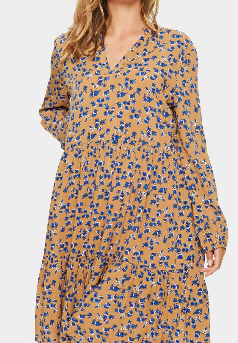 Robe à manches longues avec col en V en tissu moutarde à motif floral bleu et blanc, design à étages avec détail froncé à la taille.