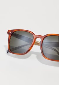 Ochelari de soare cu model țestoasă, cu lentile gri, rame groase în formă pătrată și accente metalice. Interiorul are un detaliu de design cu nuanță aurie.